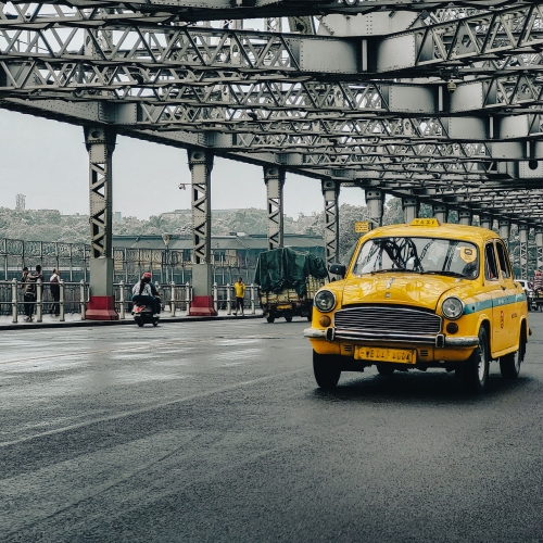 A yellow taxi cab driving down a street under a bridge.